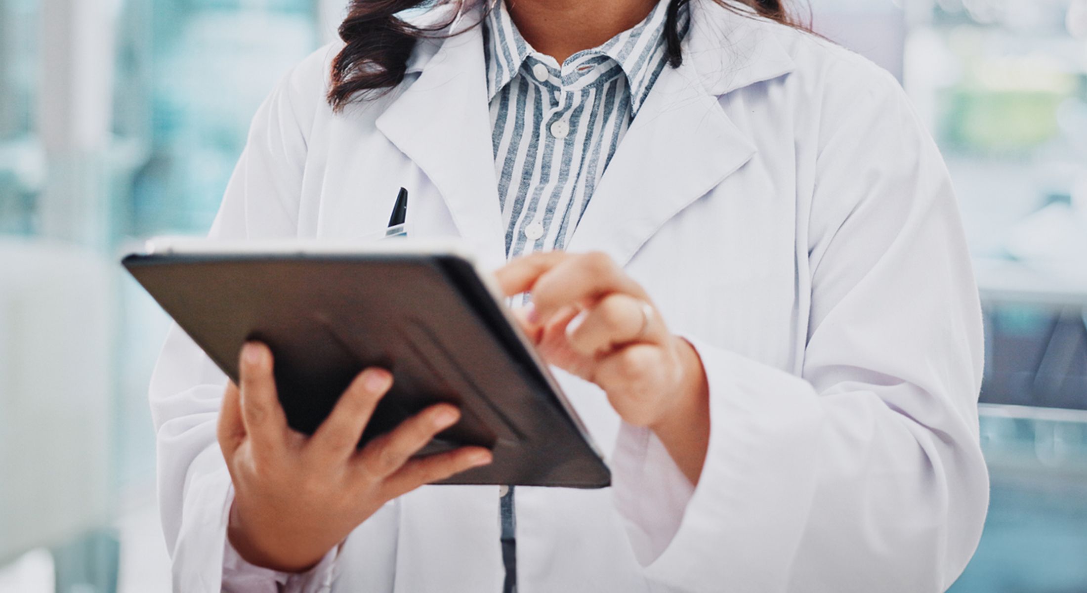 Person in lab coat using tablet device.